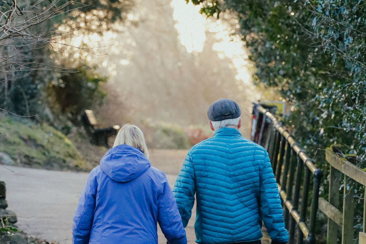 An older couple walking together along a tree-lined path